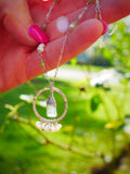 Hand holding a delicate necklace with a green pendant against a blurred green background